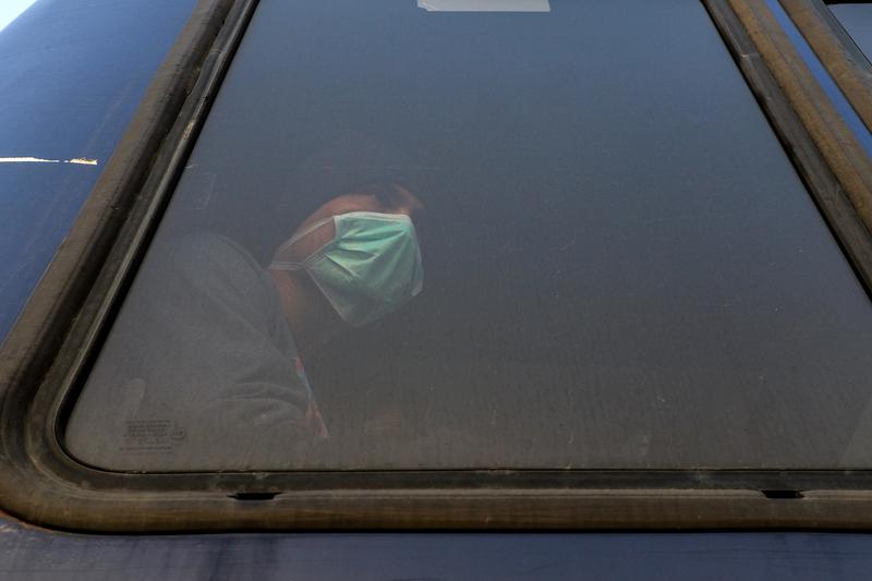 3月20日，列斯伏斯島上一名配戴口罩的難民被警方載運前往希臘本土其他難民營安置。（攝影／REUTERS／Elias Marcou／達志影像）