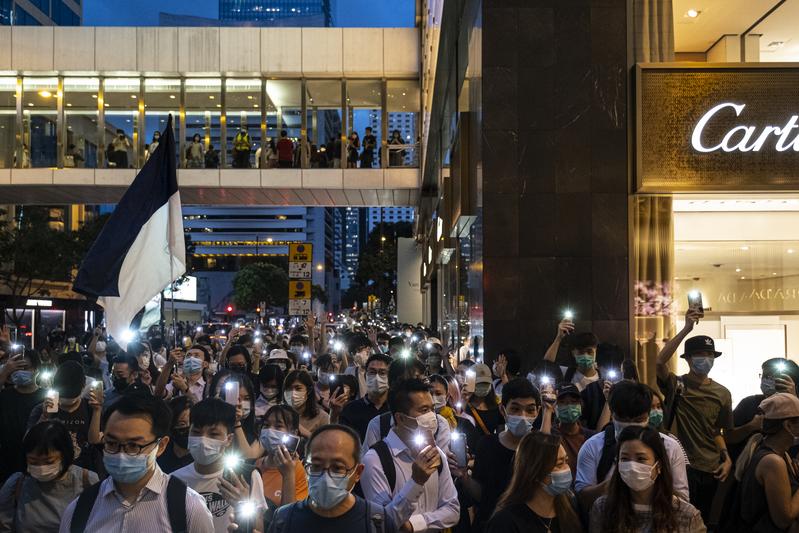 9日是香港反送中運動一週年，香港網民在網路上發起「香港人抗爭一週年港島區大遊行」，號召民眾在下班後，以流水集會的方式遊行。中環的夜晚因而閃起點點亮光，部分民眾高舉「五大訴求，缺一不可」的手勢。（攝影／陳朗熹）