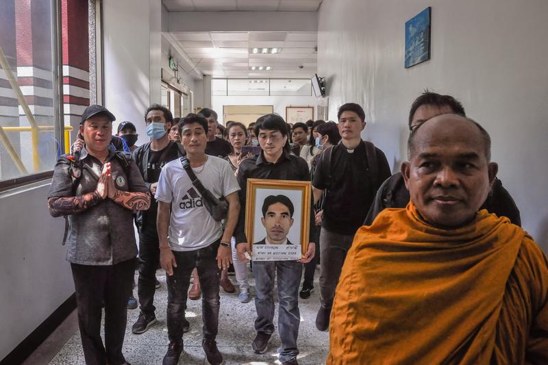 M手持父親拜倫的遺照，在泰國僧侶的引導下，將父親遺體送往火化。（攝影／簡永達）