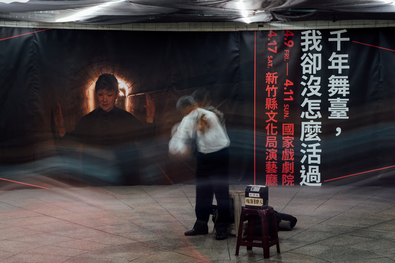 將在4月於2021台灣國際藝術節演出的《千年舞台，我卻沒什麼活過》，由具歷史視野及社會批判精神的新加坡導演王景生、台灣影像藝術家陳界仁和張照堂共同創作。圖為街頭藝人在宣傳海報前演出。（攝影／余志偉）