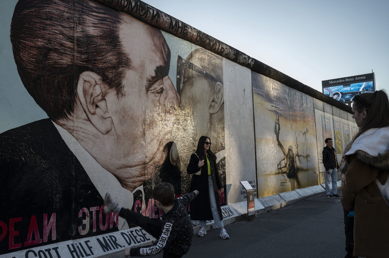 觀光客在柏林的東邊畫廊留影。這段保存至今的柏林圍牆上有許多藝術家的壁畫作品，其中一幅由弗魯貝爾（Dmitri Vrubel）創作的〈我的上帝，助我在這致命之愛中存活〉 （My God, Help Me to Survive This Deadly Love），描繪了前蘇聯領導人布里茲涅夫（Leonid Brezhnev）與前東德領導人何內克（Erich Honecker）的社會主義兄弟之吻。（攝影／楊子磊）