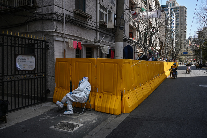 3月29日，上海靜安區一名穿著防護服的工作人員倚著用來隔離社區的牆板休息。（攝影／AFP／Hector RETAMAL）