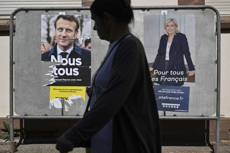 2022年大選前三天，在法國東部的米盧斯（Mulhouse），一名行人走過總統候選人馬克宏和雷朋的競選海報。（攝影／AFP／Sebastien Bozon）
