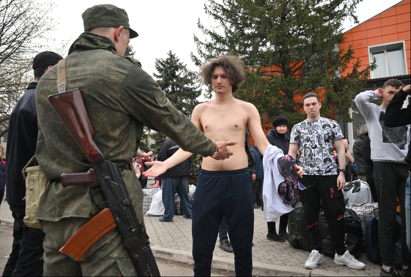 一群被俄羅斯軍隊疏散的馬里烏波爾居民，脫衣接受軍人檢查。（攝影／Sputnik via AFP／Ilya Pitalev）