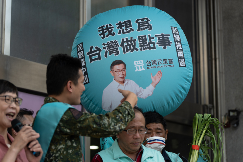 台灣民眾黨的市議員參選人受訪時，工作人員舉著的宣傳氣球上印著黨主席柯文哲的照片。（攝影／陳曉威）