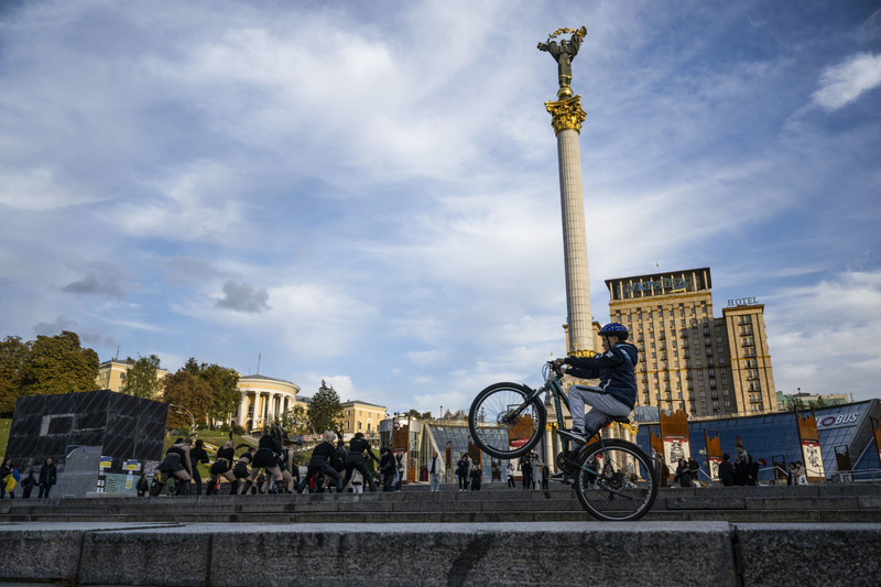 烏克蘭著名地標獨立廣場依然熱鬧，只是騎腳踏車與跳舞的人們旁，雕像（如左下方）仍被特殊的加固措施保護著，因為炸彈和無人機隨時會來。（攝影／楊子磊）