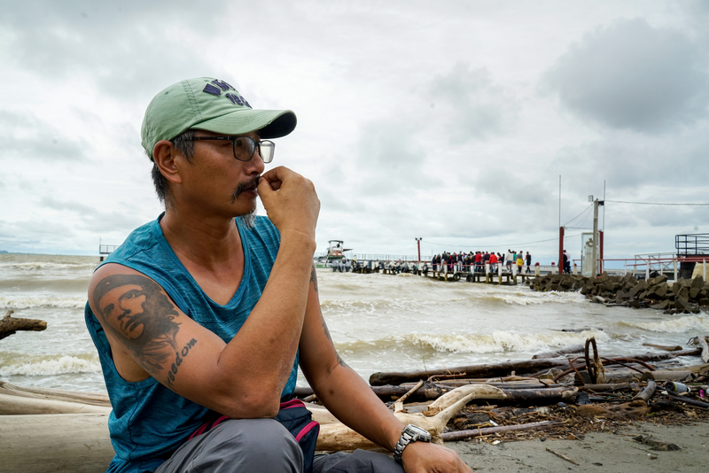 Zhou Jun, a former rights activist and card-carrying political refugee recognized by the United Nations from China’s Jiangsu province, ponders the weather, wondering if it is OK to set sail from Necoclí, Columbia. He says his tattoo of Latin American revolutionary Che Guevara symbolizes the independence and freedom he is seeking on his journey. (Credit: Chen Yingyu)