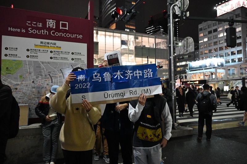 11月30日，東京新宿街頭，當地華人發起集會，關注中國烏魯木齊大火並聲援白紙運動。群眾手拿「烏魯木齊中路」，代表了上海集會後被當局拆下的路牌標誌。（圖片提供／東京白紙運動組織者）