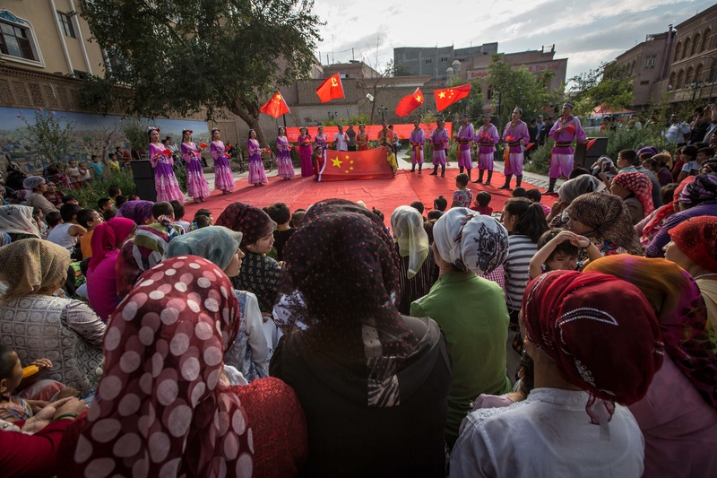 2017年7月18日，在新疆喀什街頭，維吾爾族民眾觀看身著傳統服飾的舞者在表演開始前揮舞中國國旗與中共黨旗。（攝影／SOPA Images/LightRocket via Getty Images／Guillaume Payen）