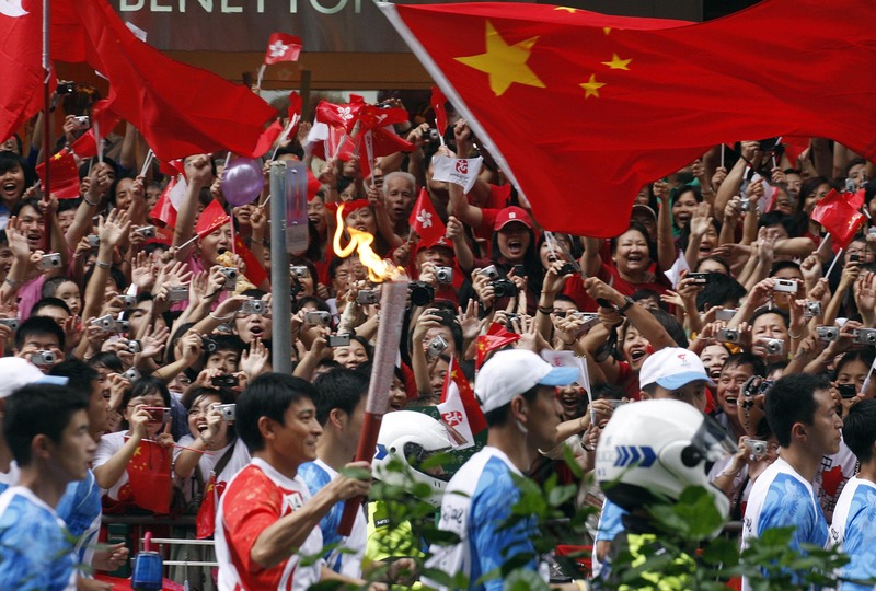 2008年5月2日，香港影星劉德華手持北京奧運聖火，經過街道邊揮舞中國國旗與香港特區旗的民眾。（攝影／AP Photo／Melanie Ko）