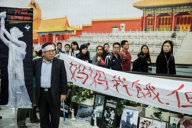 2017年1月9日，時任支聯會主席何俊仁在一面因缺乏香港社會公眾諮詢而受批評的香港故宮文化博物院廣告前，進行抗議天安門事件的活動。何俊仁在80年代初期投身政治，支持香港回歸祖國、實行港人民主治港；2020年後，多次與其他民主派人士被控違反《香港國安法》，以「組織及參與非法集會」、「煽動參與未經批准集結」等罪名遭判刑或起訴。（攝影／AFP／Isaac Lawrence）