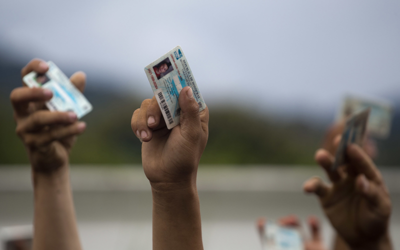 2018年，宏都拉斯移民在穿越宏都拉斯和瓜地馬拉邊境後被警方攔下時，高舉國民身分證。（攝影／AP Photo／Moises Castillo）