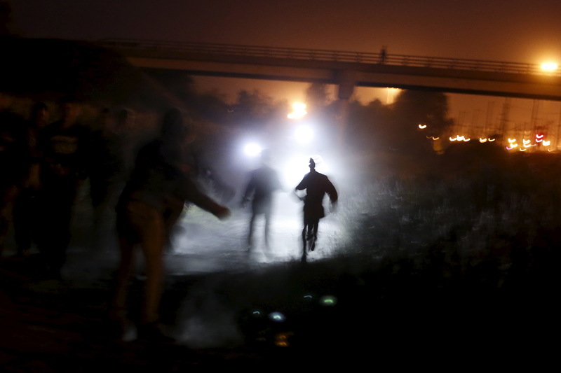 2015年8月，在法國加萊附近的弗雷坦（Frethun），一群試圖在夜裡奔跑穿過圍籬的祕密移民者被警察的手電筒照亮。（攝影／REUTERS／Juan Medina／達志影像）