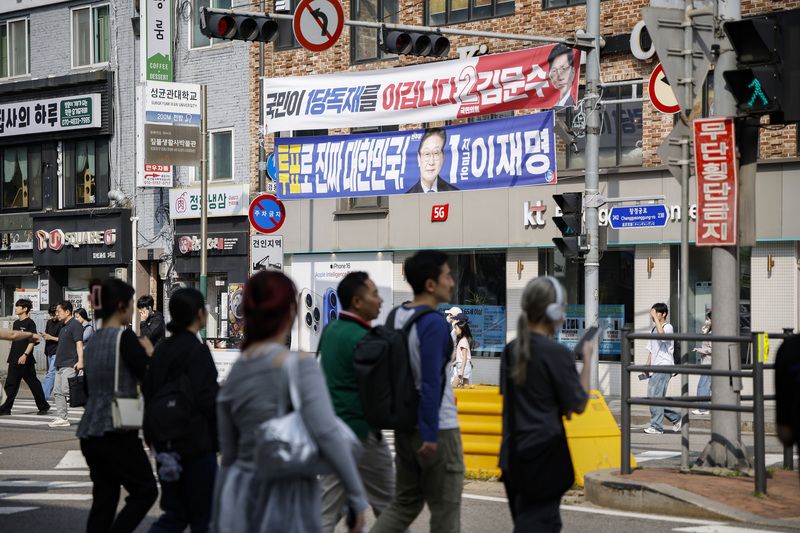2025年6月3日,韓國總統大選投票日,首爾街頭的行人走過懸掛於路口的競選布條,上方為國民力量候選人金文洙,下方為共同民主黨候選人李在明。(攝影/Woohae Cho/Getty Images)
