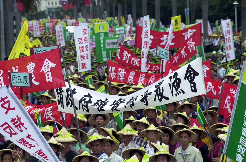 2002年11月23日,各地農民串聯集結北上台北街頭發動「1123與農共生」大遊行,抗議隊伍高舉印有各地農漁會名稱的橫幅,反對政府加入WTO(世界貿易組織),擔心將影響農漁民的權益。(攝影/Jerome Favre/AP Photo/達志影像)