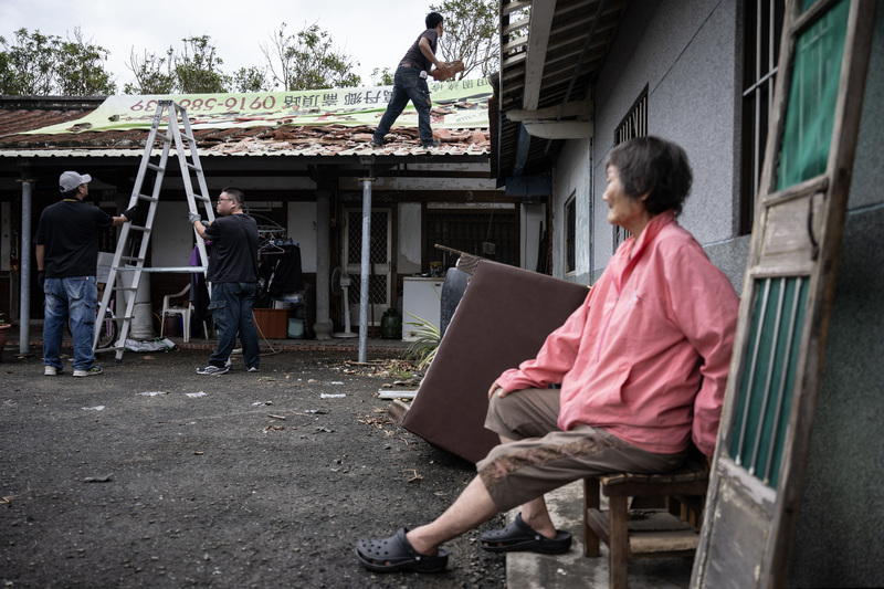 2025年7月15日，志工在學甲區三慶里協助老人將破損的屋頂蓋上防水帆布。（攝影／楊子磊）