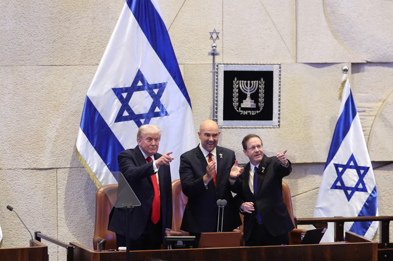 2025年10月13日，美國總統川普（左）在耶路撒冷的以色列國會（Knesset）發表演說前，接受全場起立鼓掌，身旁為以色列國會議長歐哈納（Amir Ohana，中）與總統赫佐格（Isaac Herzog）。（攝影／Evelyn Hockstein／POOL／AFP）