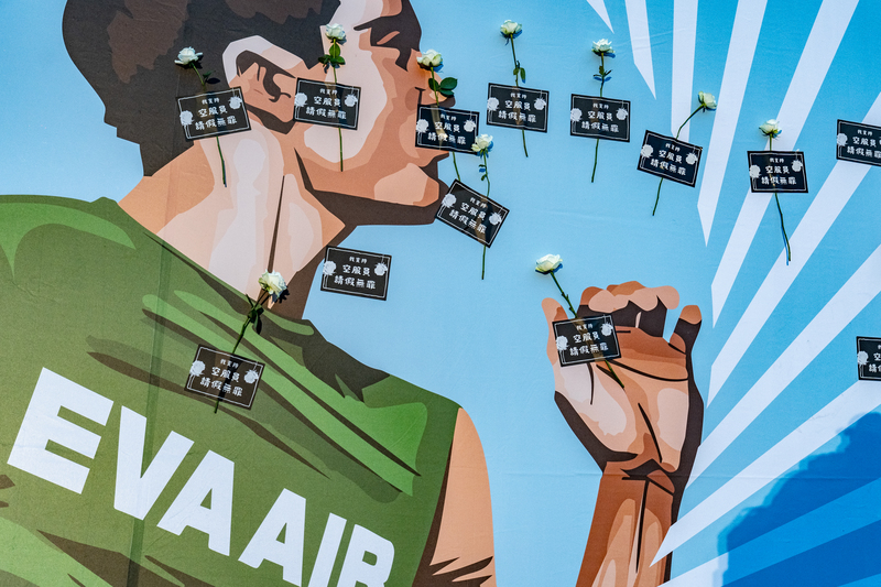 10月26日長榮航空馬拉松選手們全部起跑後,桃園市空服員職業工會成員將白玫瑰與訴求標語貼在舞台背板上。(攝影/陳曉威)