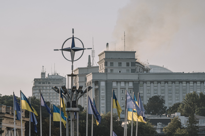 賈頓艾許在《成為歐洲人》中寫的是歐洲，更是歐洲如何從二戰廢墟中找到共同體，並在俄烏戰爭中捍衛價值。圖為2025年9月7日，在烏克蘭基輔「歐洲廣場」豎立的北約（NATO）標誌、歐盟旗與烏克蘭國旗後方，政府大樓因為俄羅斯空襲導致起火冒煙。（攝影／Andrew Kravchenko／Bloomberg via Getty Images）