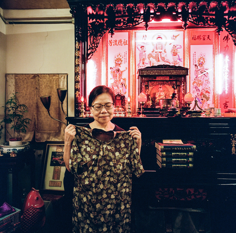 2025年6月，歷經11年抗爭和訴訟的瑠公圳迫遷案屋主賴碧珍，在強制拆除前夕接受《報導者》訪問，拿著阿媽陳罔市的旗袍站在客廳神明桌旁。之後，6月25日台北地方法院指出因債務人向新北市政府文化局申請古蹟審議，而取消隔日的強制執行。（攝影／楊子磊）