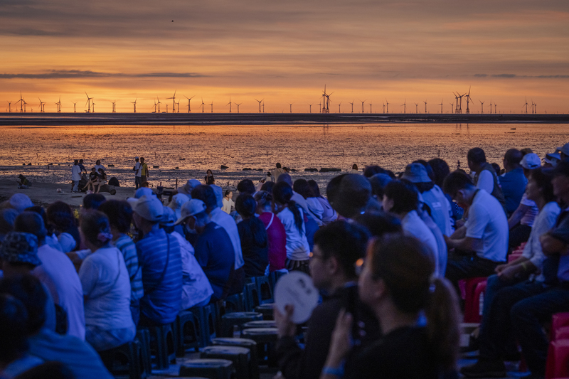 8月9日，夕陽入海前，晚霞映照在彰化芳苑的潮間帶，參加「潮芳苑｜看見灘地藝術季」的觀眾，注視著泥灘地舞台上，當地素人搬演關於海與人的故事。（攝影／馬雨辰）