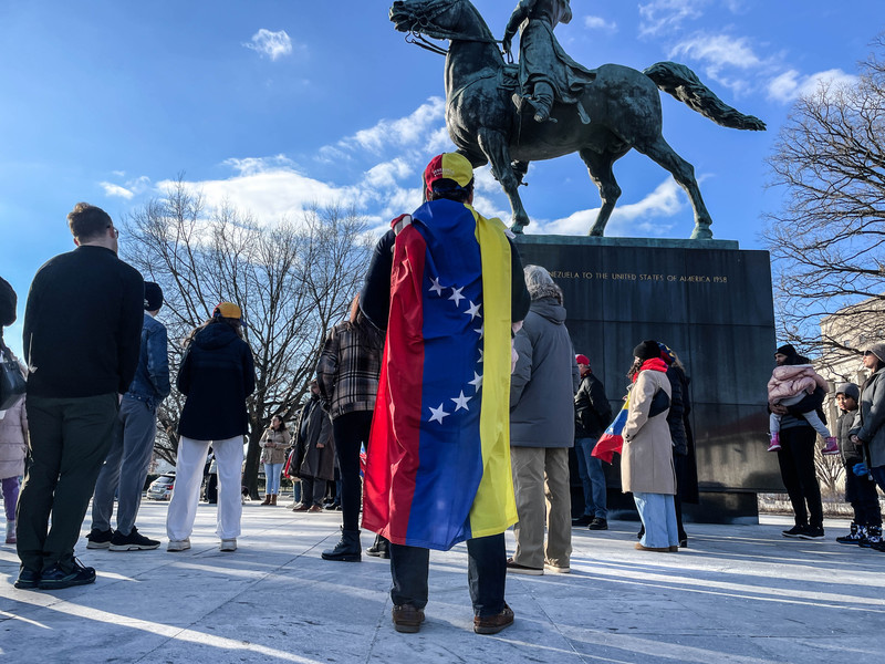 1月4日,32歲的安利格(Enrique)身披委內瑞拉國旗,帶著妻子與3個月大的孩子參加慶祝美國逮捕馬杜洛的華府集會。(攝影/陳映妤)