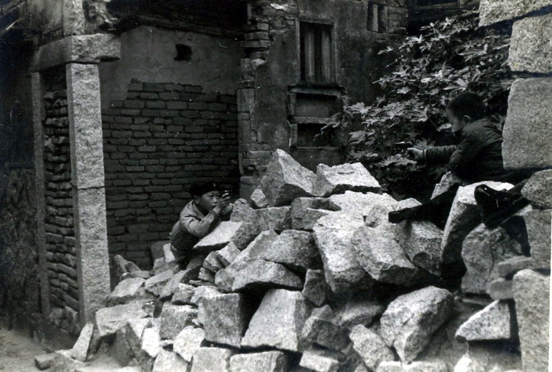 李根政：「這張照片的時間是1973年，兩個哥哥在金門老家隔壁被炮火摧毀倒下的石堆中，玩著打仗遊戲。我當時只有5歲，可能沒有參加這場遊戲。照片的攝影者是我的三叔，使用的是東德Praktica單眼相機。當時三叔將鏡頭和機身分開攜帶，躲過安檢，帶回金門。三叔還有一台德製120底片蛇腹相機，我的父親（三叔的大哥）因為害怕被憲兵臨檢，情急之下丟到家前的池塘。」（攝影／李沃植）