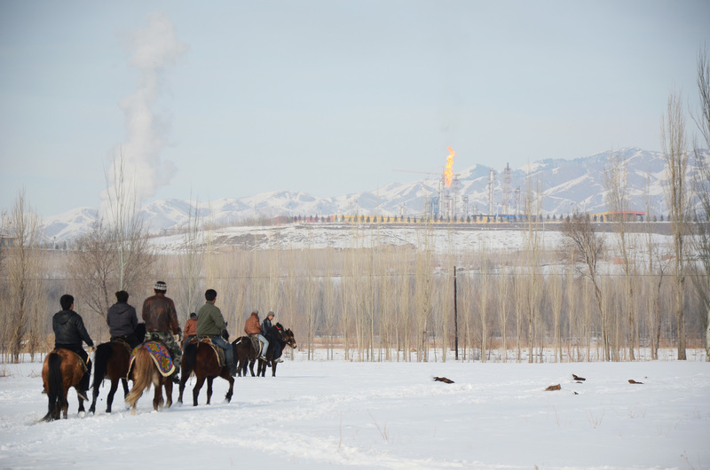 為滿足沿海城市對空氣品質與能源的需求，中國政府在西部大量建設燃煤電廠。圖為2014年1月，新疆楚魯海（Chuluqay）的村民們正在賽馬，背景矗立著中國慶華能源集團（China Kingho Energy Group）的煤炭氣化廠。（攝影／Benjamin Haas／Bloomberg via Getty Images）