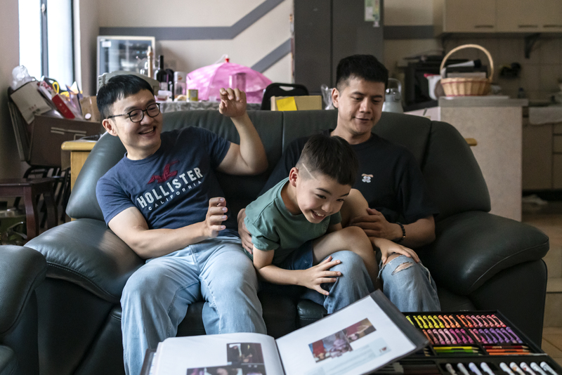 Sean(左起)、飛海、Eddie共組的小家庭。桌上擺放的資料夾,記錄飛海來到世界的過程,包括幫助他來到這個家的「捐卵阿姨」、「代理孕母阿姨Sloane」相關資訊。(攝影/陳曉威)