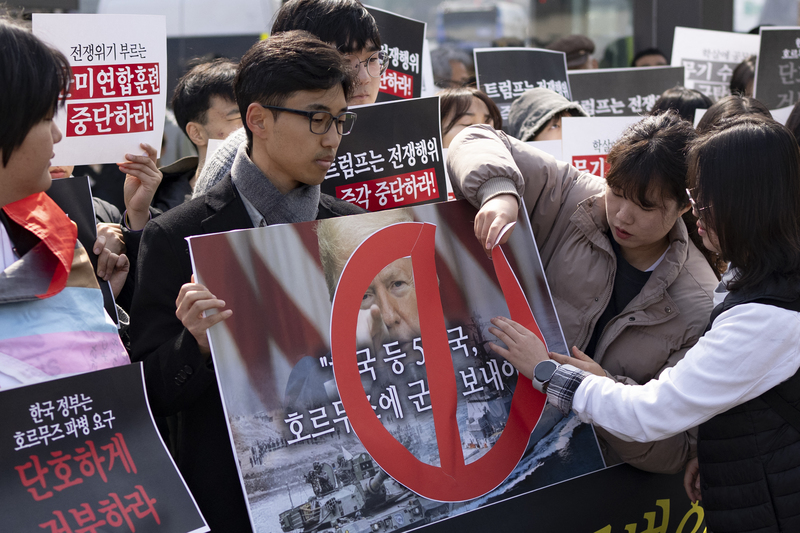 2026年3月16日，韓國首爾光化門廣場，在一場反戰與呼籲停止美韓聯合軍演的集會中，抗議者將紅色禁止標示貼在印有川普相片的海報上。（攝影／Chris Jung／NurPhoto via AFP）