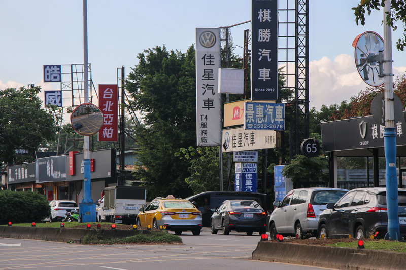 台北濱江街一帶，路邊立牌一字排開，從各大車系的招牌、保修廠看板，到鈑金、烤漆、輪胎與材料行，隔著一條車道相望。（攝影／徐孜儀）