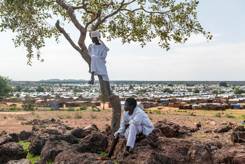 兩名來自蘇丹西達佛州（West Darfur）的男孩，坐在查德阿博滕格（Aboutengue）難民營附近的岩丘上眺望。這座營地收容了數以萬計越境逃離的蘇丹平民。照片攝於2025年7月25日，查德。（攝影／Moises Saman／Magnum Photos；照片提供／無國界醫生）