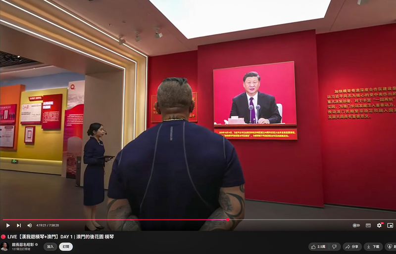 2025年8月18日，館長在鄰近澳門的橫琴參訪時，特意停留在習近平的畫像前，雙手交叉在背後聆聽這位中國領導人對一國兩制的規畫。（圖片來源／館長惡名昭彰頻道／YouTube平台截圖）