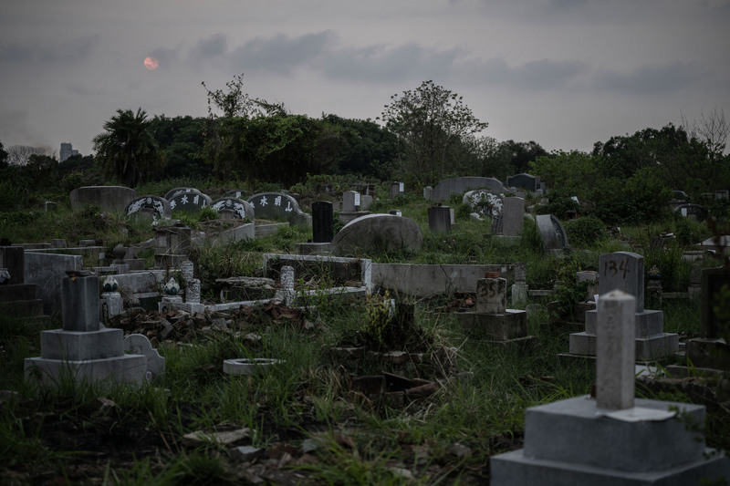 2026年3月28日，日落時分的南山公墓B區。大量墓碑被以矽利康黏貼官方查估文件，部分甚至可以看見早期留下的噴漆標記。（攝影／楊子磊）