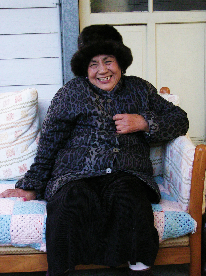 2009年，坐在自己鉤織的沙發墊上，達邦老家前的菊花阿姨對紀錄片團隊露出笑容。（圖片提供／野火樂集）