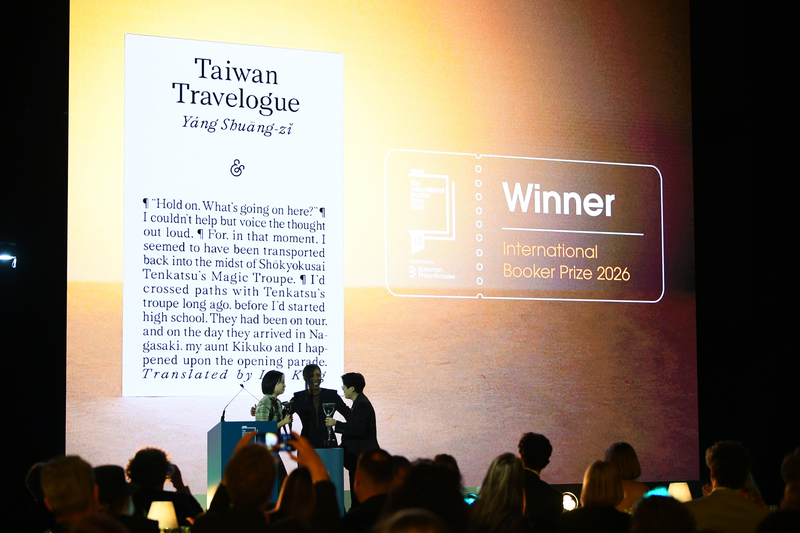 倫敦頒獎典禮現場大螢幕投射出《Taiwan Travelogue》的書影，作家楊双子（右）與譯者金翎（左）在眾人矚目中登台，拿起獎座與評審團主席（中）合影。（攝影／Joe Maher／Getty Images）